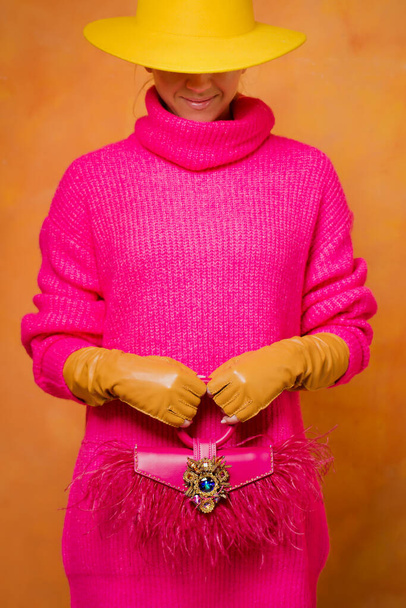 Fashionista σε καυτό ροζ πουλόβερ, δερμάτινα γάντια με ροζ τσάντα με φτερά στρουθοκαμήλου - Φωτογραφία, εικόνα