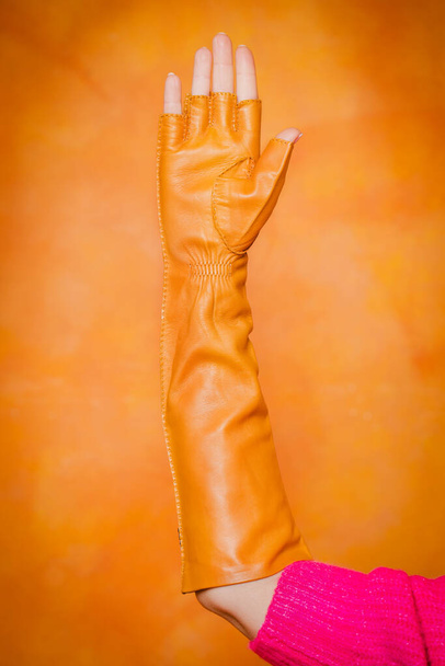 Žluté dlouhé rukavice s rukavicemi na ženské ruce na oranžovém pozadí - Fotografie, Obrázek