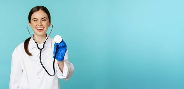 Image of woman doctor, listening patient lungs with stethoscope, doing medical checkup in clinic, standing over blue background. - Φωτογραφία, εικόνα