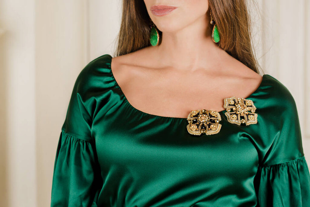Een mooie vrouw in een groene zijden jurk met broches gemaakt van kralen - Foto, afbeelding