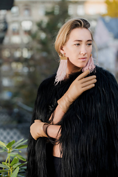A beautiful woman in a fur coat, with ostrich feather earrings and beige leather gloves - Photo, Image