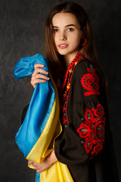 Een mooie Oekraïense vrouw in een nationale Oekraïense jurk met een blauwe en gele vlag van Oekraïne - Foto, afbeelding