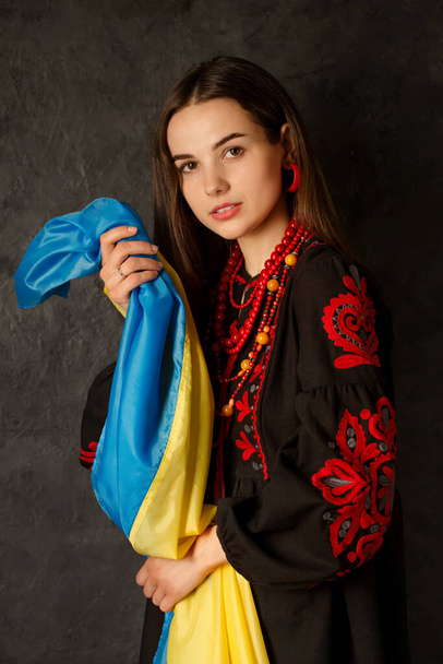 Μια όμορφη Ουκρανή γυναίκα σε ένα εθνικό ουκρανικό φόρεμα με μπλε και κίτρινη σημαία της Ουκρανίας - Φωτογραφία, εικόνα