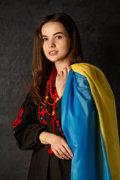 Eine schöne ukrainische Frau in einem ukrainischen Nationalkleid mit einer blau-gelben Flagge der Ukraine - Foto, Bild