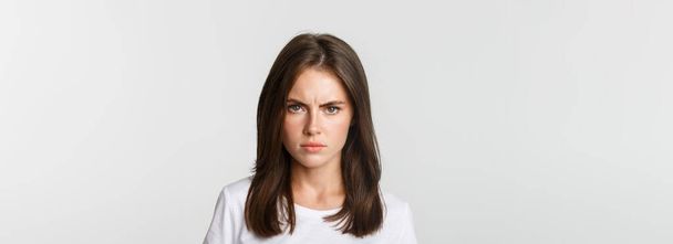 Close-up of pissed-off young girl frowning and looking angry at camera, white background. - Photo, image