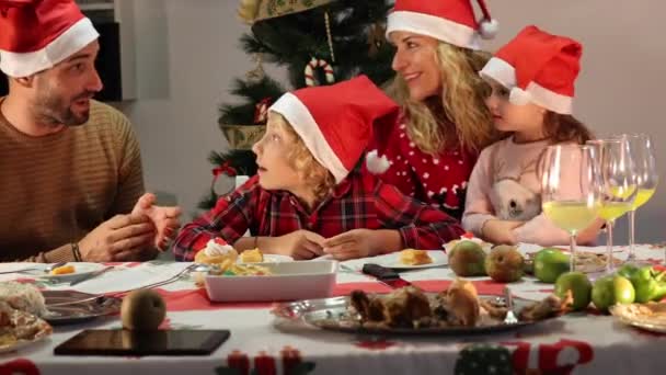 Gelukkige blanke familie met kerstmutsen die lachen en kerstdiner vieren. Vader, moeder, zoon en dochter. - Video