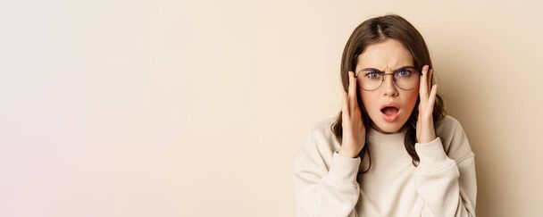 Close up portrait of woman in glasses looking confused and frustrated, cant understand smth strange, standing over beige background. - Fotó, kép