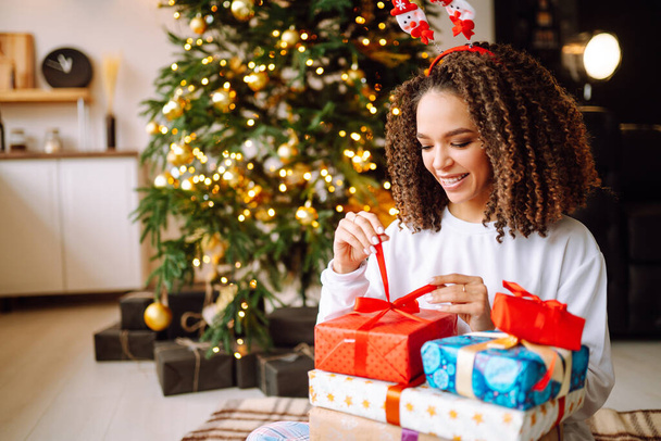 Giovane bella donna bruna sorridente con una scatola regalo in interni decorati con albero di Natale. Anno nuovo.  - Foto, immagini