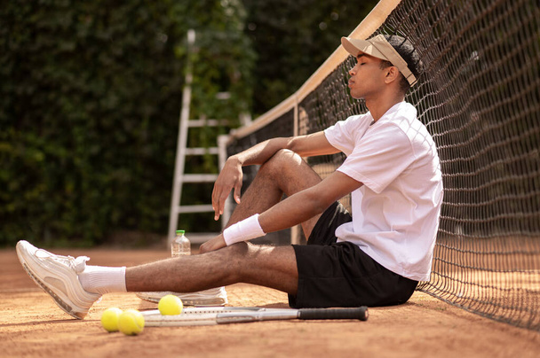 Resting. Young man sitting at the tennis court and resting - Fotoğraf, Görsel