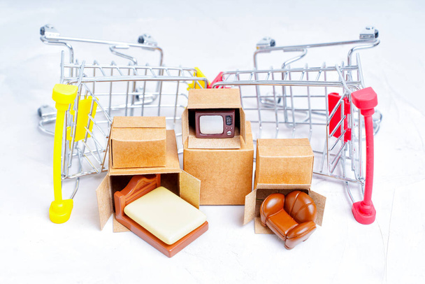 Unpacked tiny delivery boxes with miniature furniture figurines by small push trolleys isolated on white background. Renting furniture for a new apartment. - Φωτογραφία, εικόνα