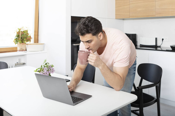 Молодий бізнесмен працює на ноутбуці і п'є чай вдома. Концепція дистанційної роботи
 - Фото, зображення