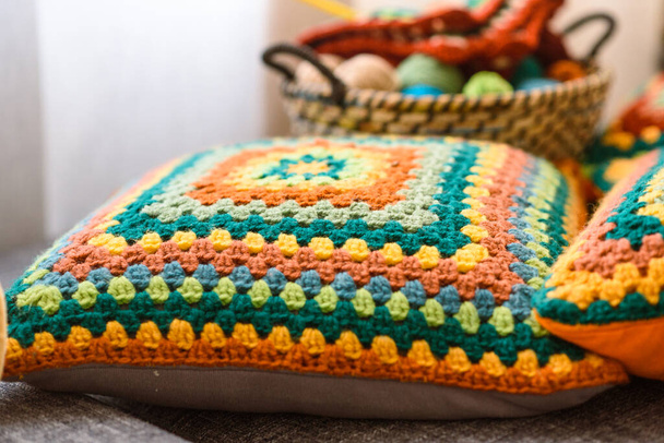 Granny square crochet. Home made creations. Colorful wool yarns in a straw basket on a couch. Handmade knitting, knit pillows, and a cute atmosphere. - Fotó, kép