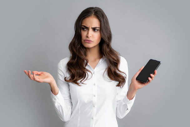 Sad woman with smart phone. Young woman with mobile phone. Serious business woman with smartphone on grey background - Foto, imagen