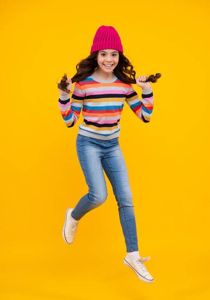 Moda mujer joven feliz en sombrero de punto y suéter que se divierten sobre fondo azul colorido. Salta y corre. Adolescente feliz, emociones positivas y sonrientes de la chica adolescente - Foto, Imagen
