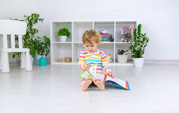 The child is looking at a book in the room. Selective focus. Baby. - Photo, Image