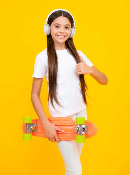 Happy teenager portrait. Fashion teenage lifestyle, beautiful teen girl with skateboard and headphones isolated on studio background. Smiling girl - Fotó, kép