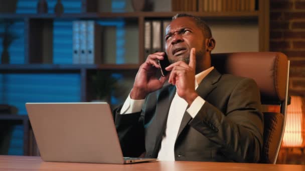 Успішний бізнесмен, сидячи в офісі, розмовляє з клієнтом на мобільному телефоні на робочому місці афроамериканський чоловік, відповідаючи на бізнес-дзвінки, емоційно спілкується за допомогою смартфона, пояснюючи переваги пропозиції
 - Кадри, відео