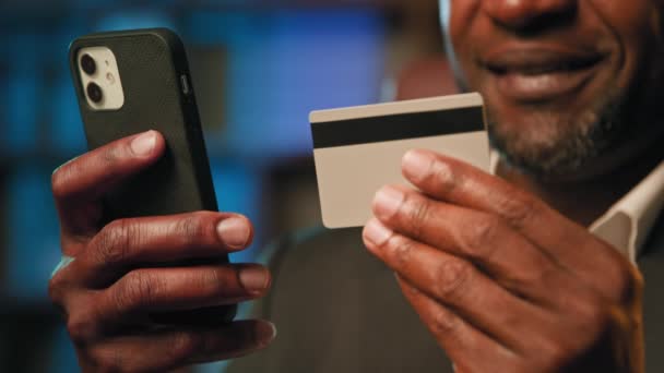Close-up male hands holding credit card and phone unrecognizable man makes purchase in online store remote pays using mobile banking application instant safe distance payment modern technology concept - Footage, Video