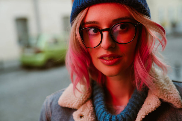 Young white woman in eyeglasses posing and looking aside on city street - Fotó, kép