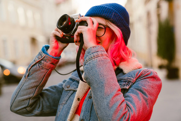 Mujer joven tomando fotos en cámara retro mientras camina en la calle de la ciudad - Foto, Imagen