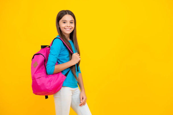 Vrolijk tienerportret. Schoolmeisje in schooluniform met schooltas. Schoolkind, tiener student houdt rugzak op gele geïsoleerde achtergrond. Lachend meisje - Foto, afbeelding