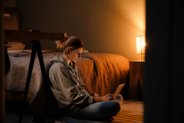 Fehér lány alagút gyűrűk segítségével laptop, miközben ül a padlón otthon - Fotó, kép