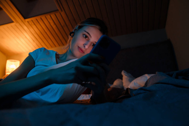 Beyaz kız evde yatakta dinlenirken cep telefonu kullanıyor. - Fotoğraf, Görsel