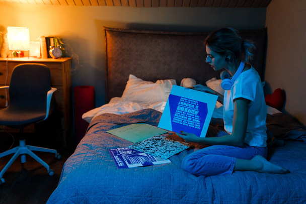 White girl sitting with vinyl records and headphones on bed at home - Foto, imagen