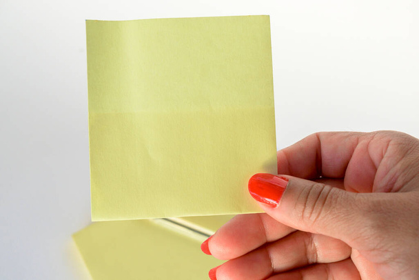 Γυναικείο χέρι με ζωγραφισμένα νύχια που κρατά λευκό χαρτί γράμμα σε καθαρό λευκό φόντο. - Φωτογραφία, εικόνα