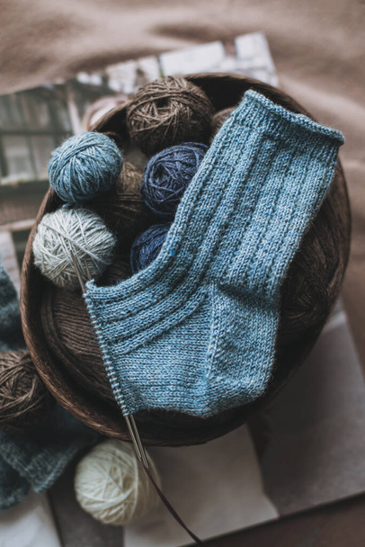 バスケットに針と糸玉で編んだ靴下を手で編む。手作りと巨大なスローライフのための概念. - 写真・画像