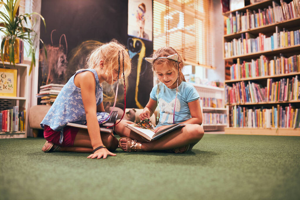 Two primary schoolgirls doing homework in school library. Students learning from books. Pupils having fun in library. Back to school - Фото, изображение