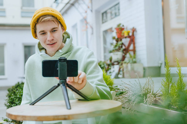 Mladý muž blogger dělat vlog pomocí smartphone sedí venku. Selektivní zaměření. - Fotografie, Obrázek