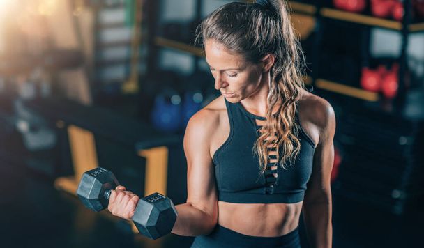 Naisurheilija tekee Biceps liikuntaa käsipainoilla. Voimaharjoittelu. - Valokuva, kuva