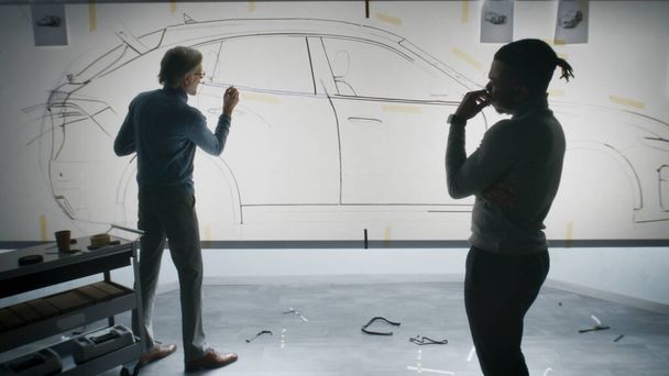 2人の多様な車の男性デザイナーがホワイトボード上で未来的な電気自動車の未来のデザインを開発し、マーカーで描く、スケッチを議論しました。彼らは現代の車の設計開発スタジオで働いています. - 写真・画像