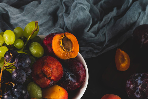 Freshly washed fruits with water droplets. bright high key look conveys freshness. Variety of fresh grapes, apricot and plumes on dark background. Fruit sources of vitamins - Foto, Imagem
