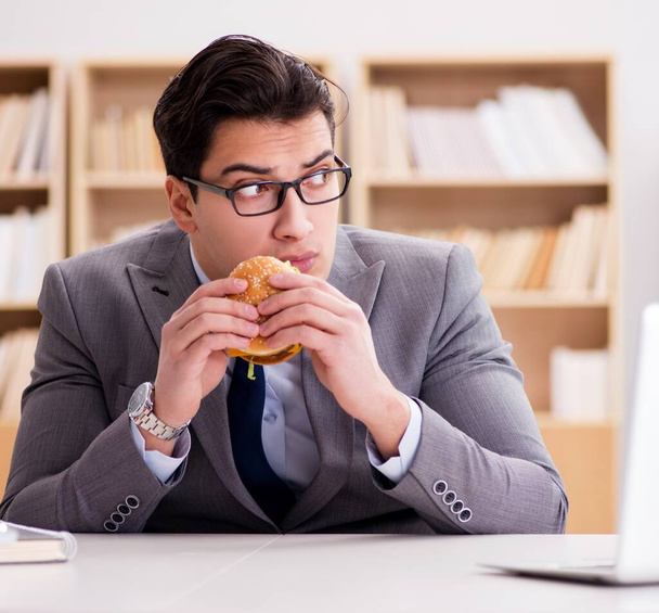 Голодный веселый бизнесмен ест сэндвич с нездоровой едой - Фото, изображение