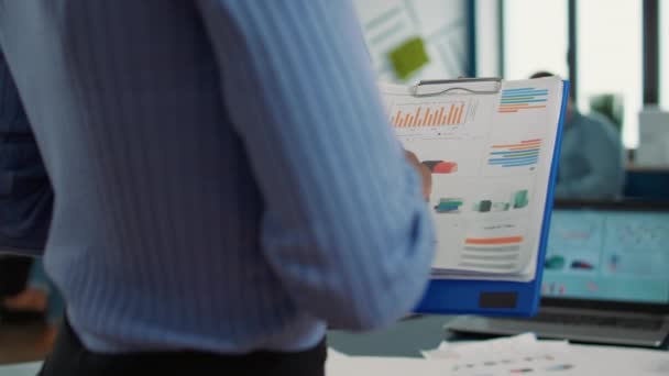 Closeup of african american woman hands holding clipboard with financial data and sales charts in startup office. Focused employee analyzing performance indicators reading business statistics. - Filmmaterial, Video