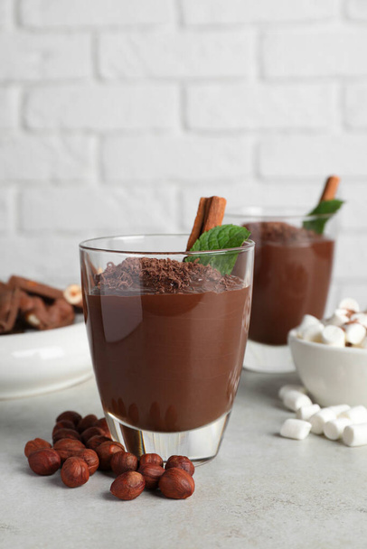 Cups of delicious hot chocolate with cinnamon stick, mint and hazelnuts on light grey table near brick wall - Φωτογραφία, εικόνα