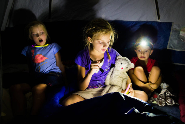 Niños pequeños en una tienda leyendo historias aterradoras en la oscuridad - Foto, imagen