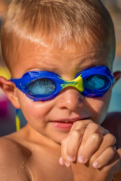 Χαριτωμένο αγοράκι που φοράει μπλε γυαλιά στην πισίνα και τρέμει. - Φωτογραφία, εικόνα