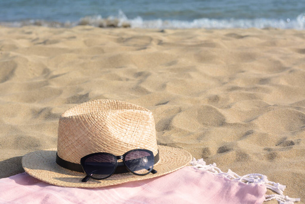 Hat with beautiful sunglasses on blanket near sea, space for text - Foto, Imagem