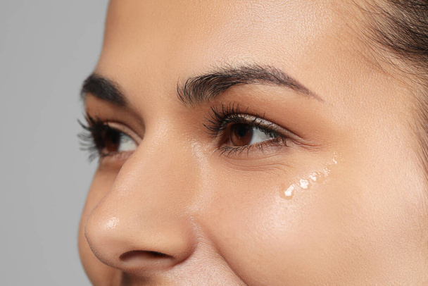 Woman with eye cream on grey background, closeup. Skin care - Foto, Imagen