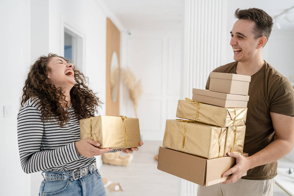 nő fiatal felnőtt kaukázusi nő áll otthon ajándékdobozzal ajándékok kezében, míg a barátja vagy férje férfi ad dobozok boldog mosoly valódi emberek ünneplik meglepetés koncepció - Fotó, kép