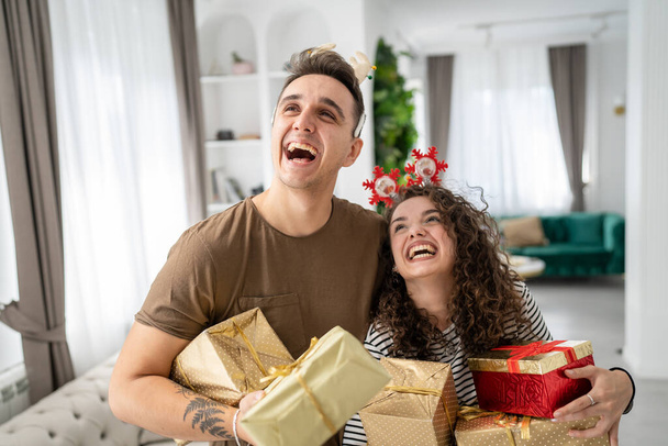 nainen nuori aikuinen valkoihoinen nainen seisoo kotona lahjapakkaus esittelee pitämällä käsissä, kun hänen poikaystävänsä tai miehensä mies antaa laatikot onnellinen hymy oikeat ihmiset juhlivat yllätys rakkaus käsite - Valokuva, kuva