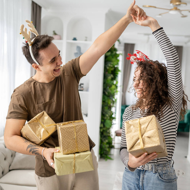 nainen nuori aikuinen valkoihoinen nainen seisoo kotona lahjapakkaus esittelee pitämällä käsissä, kun hänen poikaystävänsä tai miehensä mies antaa laatikot onnellinen hymy oikeat ihmiset juhlivat yllätys rakkaus tanssi - Valokuva, kuva