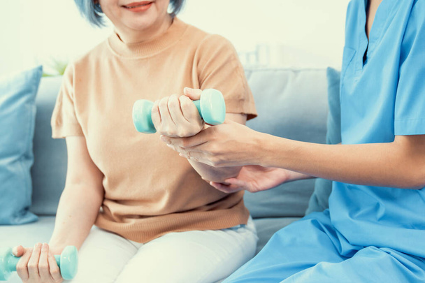 Caregiver helping contented senior woman exercise with dumbbell at home. Rehab for elder, senior medical care. - Fotoğraf, Görsel