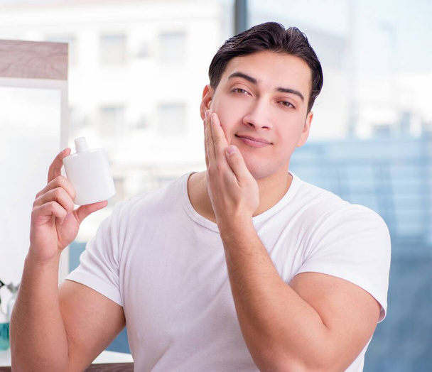 El joven hombre guapo aplicando crema facial - Foto, Imagen