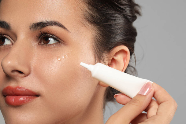 Woman applying cream under eyes on grey background, closeup. Skin care - Photo, image