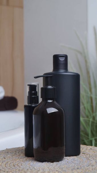 Μπουκάλι αφρόλουτρο και καλλυντικά προϊόντα σε ψάθινο τάπητα κοντά μπανιέρα σε εσωτερικούς χώρους - Φωτογραφία, εικόνα