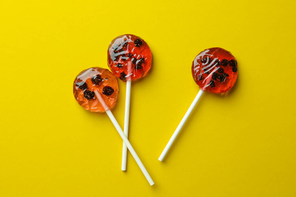 Sweet colorful lollipops with berries on yellow background, flat lay - Photo, Image